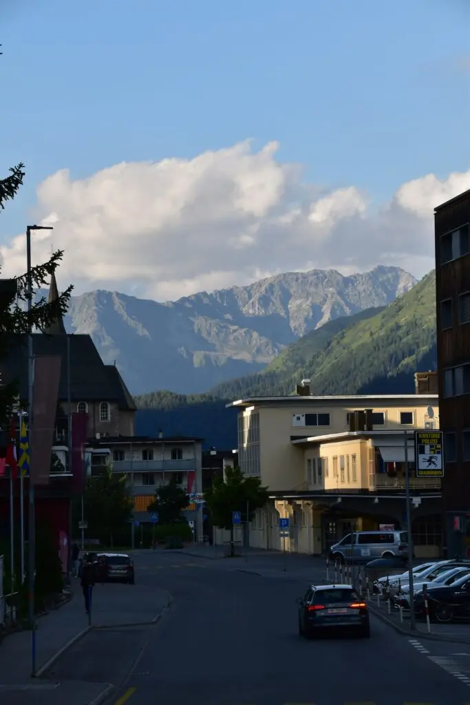 Straßenzug in einer Bergstadt mit Blick auf schroffe Alpengipfel im Hintergrund