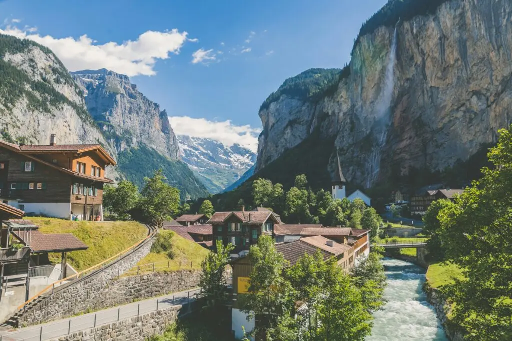 Malerisches Schweizer Bergdorf Lauterbrunnen im Tal mit Fluss, Holzchalets und Wasserfall an der Felswand