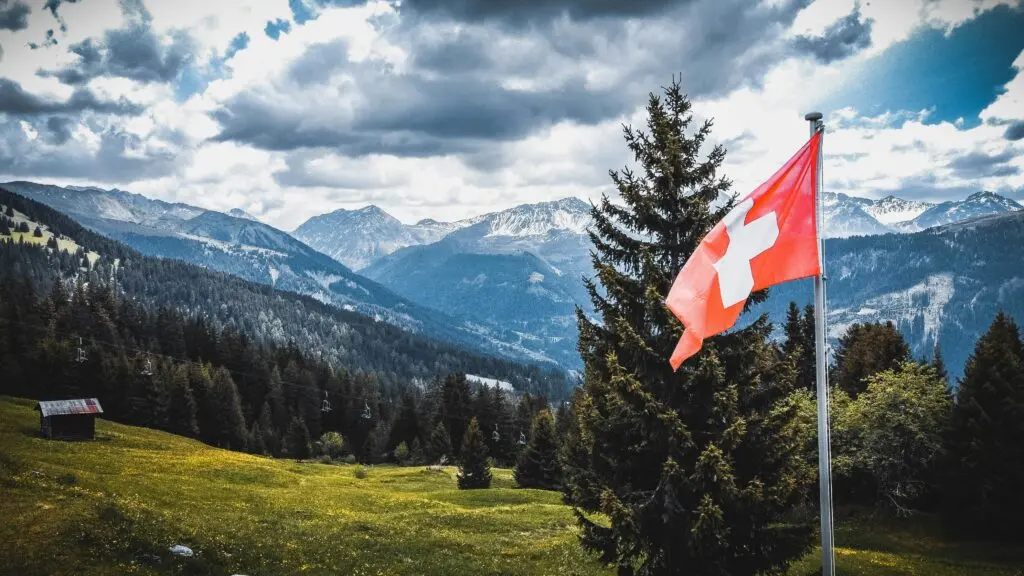 Schweizer Flagge vor alpiner Berglandschaft – Symbol für den Schweizer Immobilienmarkt und die hedonische Bewertungsmethode